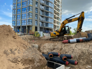 Excavator performing underpinning on an existing foundation to structurally enhance the foundation for a condo development
