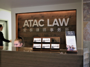Inside the office of Vancouver law firm ATAC Law. Receptionist seen behind a large wooden counter with a large wooden sign behind her reading ATAC LAW in big bold letters.