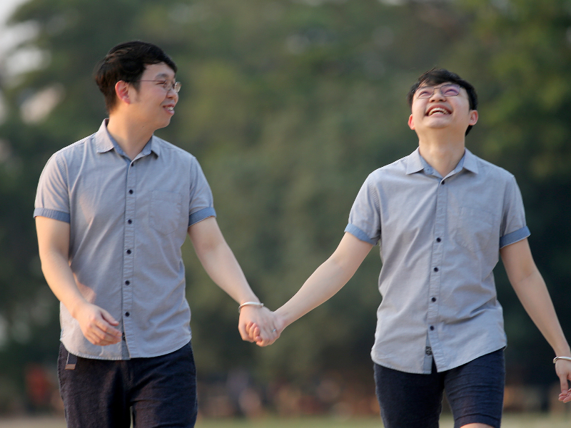 2 gay asian men holding hands and smiling after coming to Canada where they can embrace their same sex relationship without breaking the law.